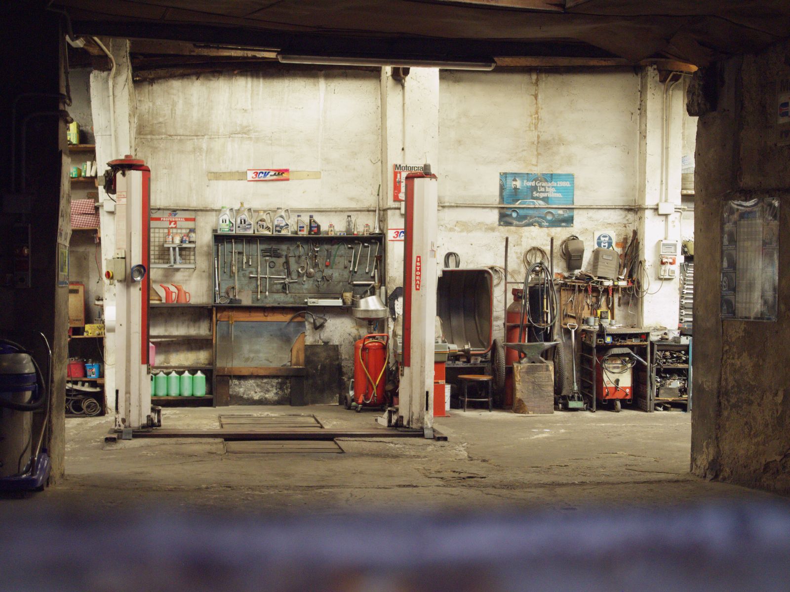 Uma oficina mecânica vazia e rústica, com ferramentas, máquinas e elevadores de automóveis em um ambiente industrial.